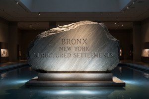 a granite slab with the words Brobnx NY structured settlement chiseled in on a pedestal in a museum reflecting pool